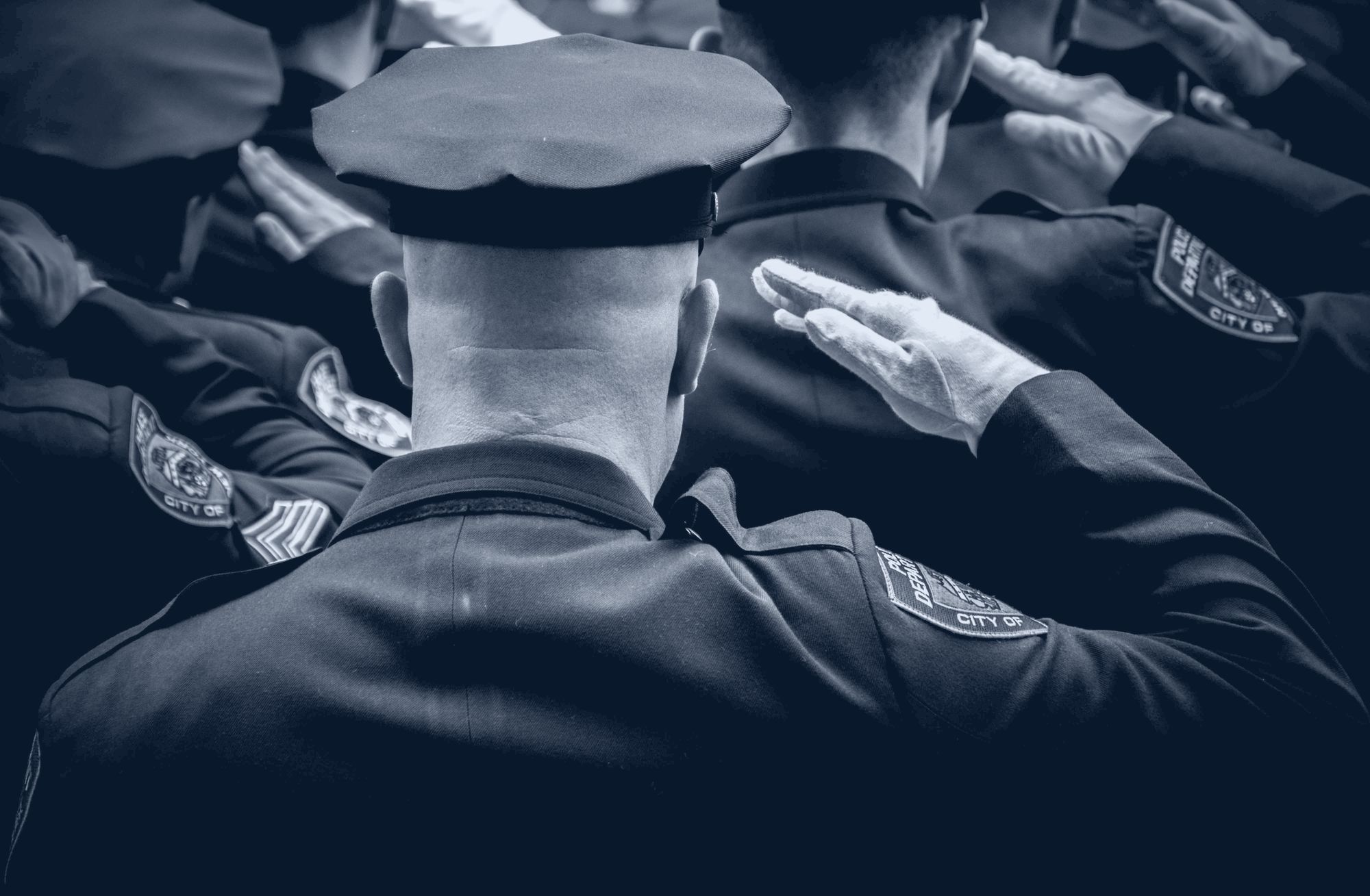 Uniformed police officers saluting in formation, seen from behind