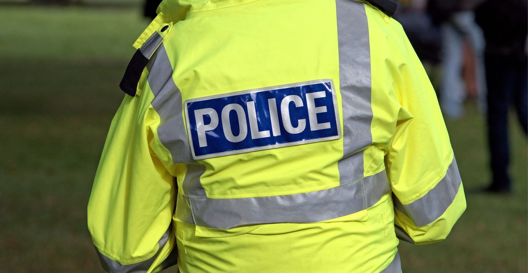 A police officer in a high-visibility jacket marked POLICE, seen from behind